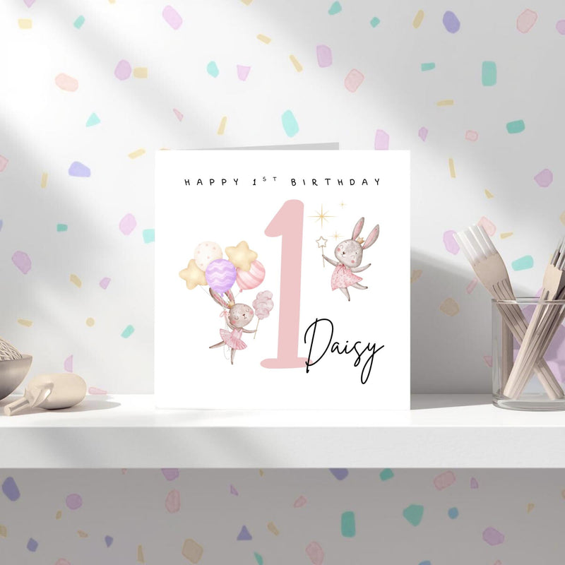May include: A birthday card with the text "Happy 1st Birthday" and the name "Daisy". The card features illustrations of bunnies, balloons, and the number 1 in pink.